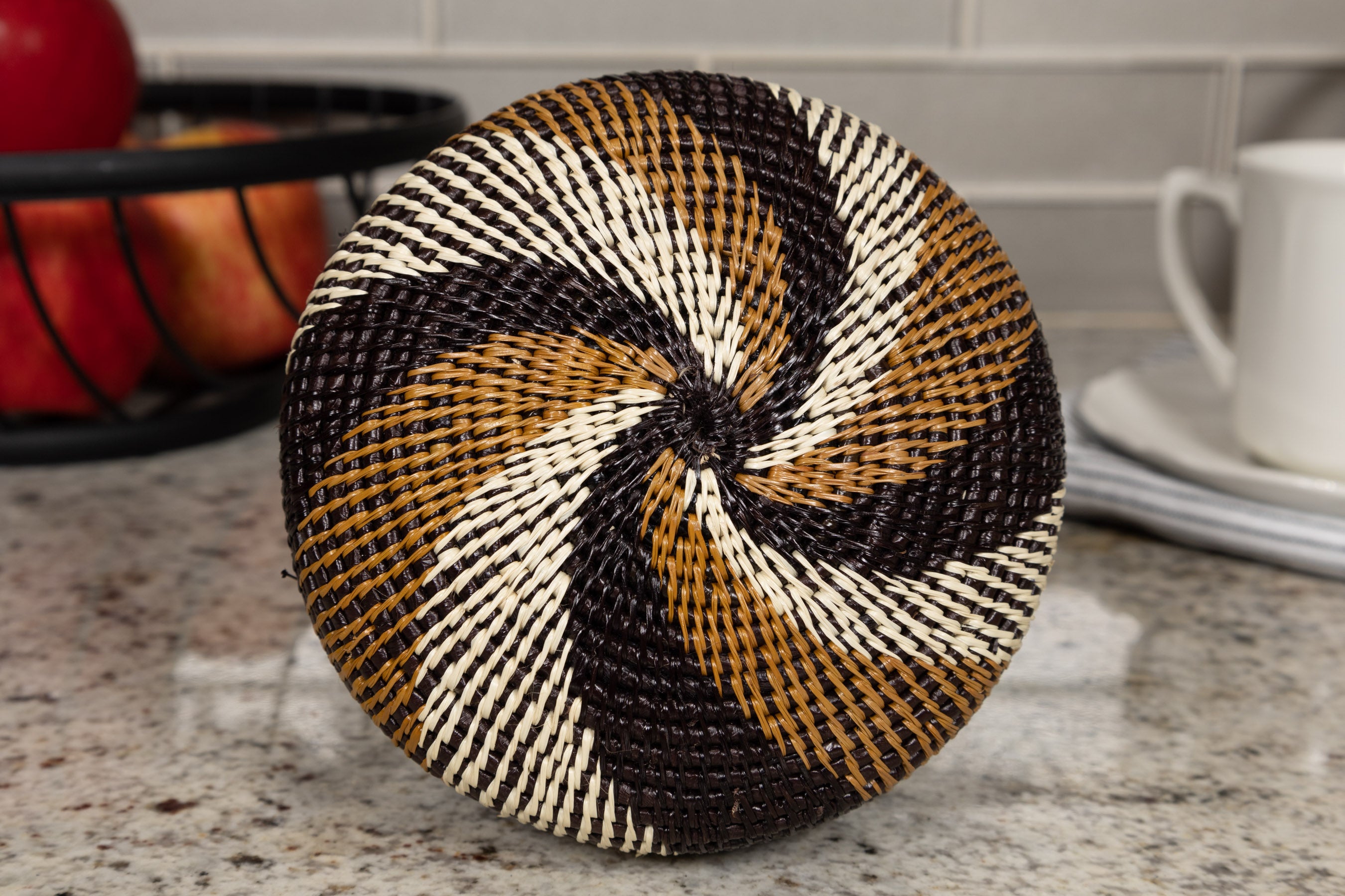 Round woven basket bottom with black, brown, and beige pattern on a kitchen counter.