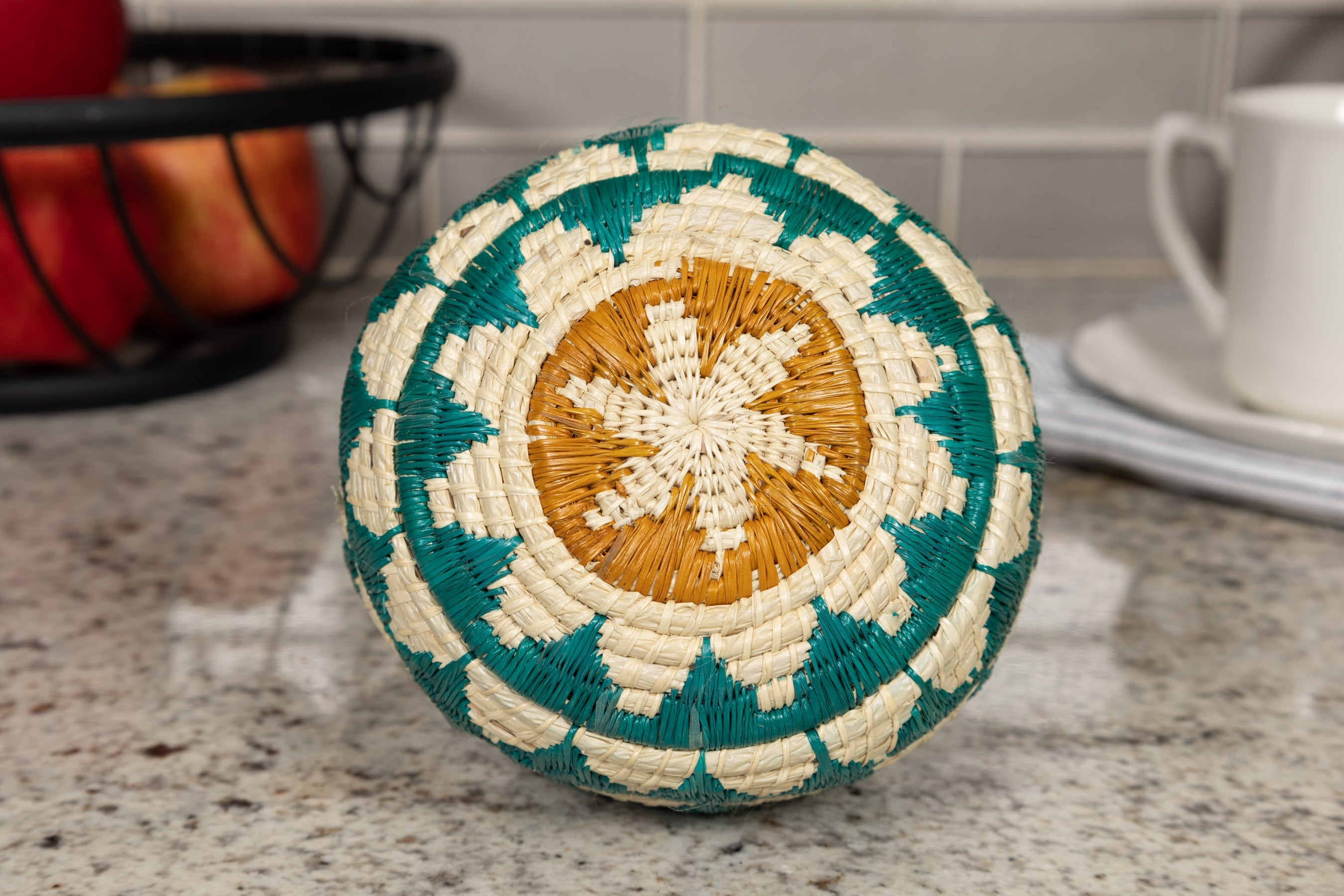 Decorative woven ball with tourquise blue, beige, and brown pattern on a kitchen counter.