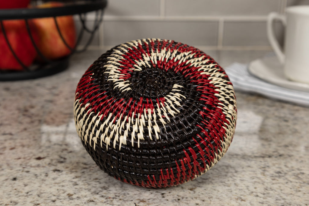 Round woven basket with black, red, and beige pattern on a kitchen counter.