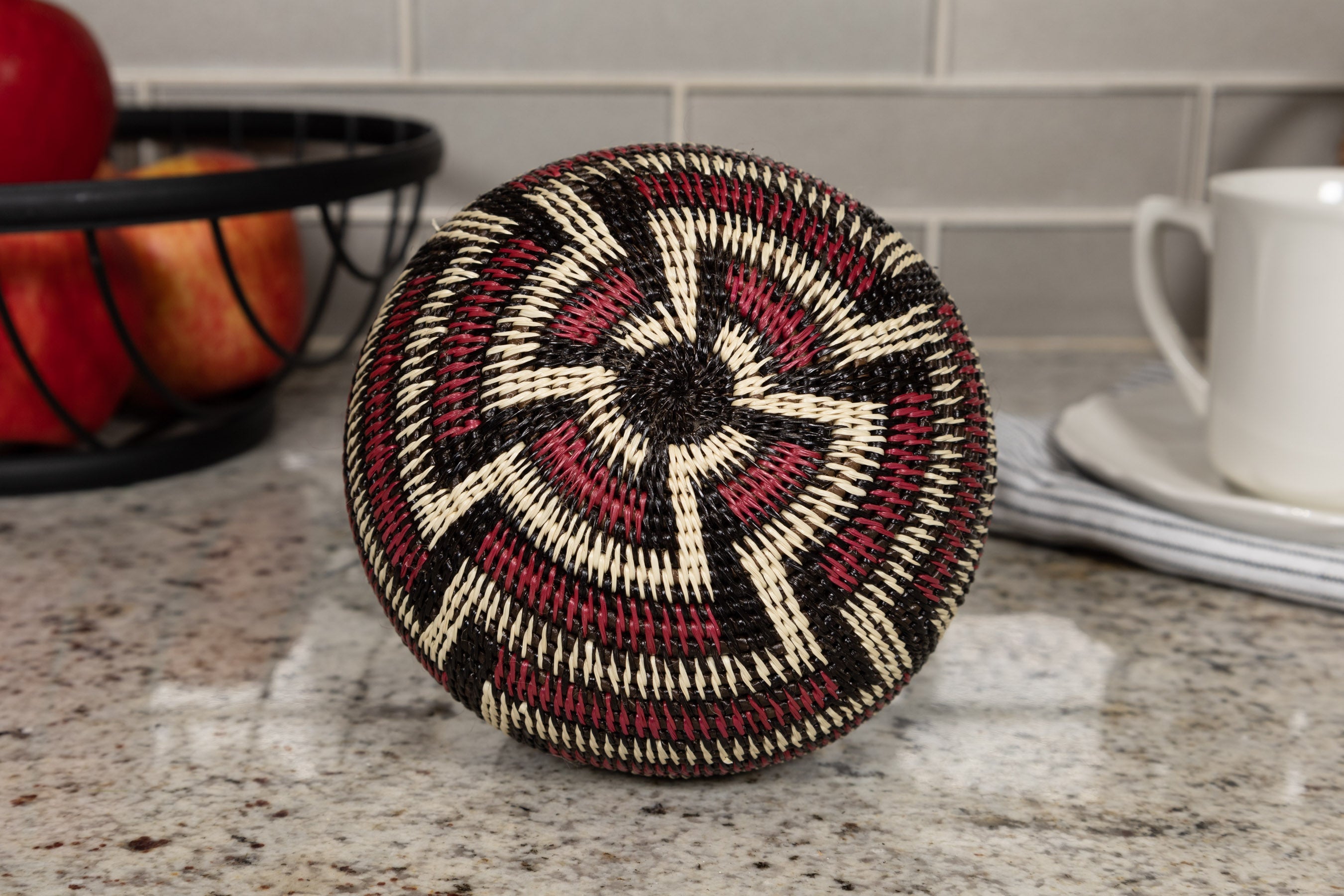 Decorative woven basket on a kitchen counter with apples and a mug in the background