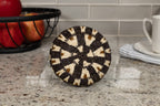 Decorative woven basket bottom on a kitchen counter with apples and a mug in the background.