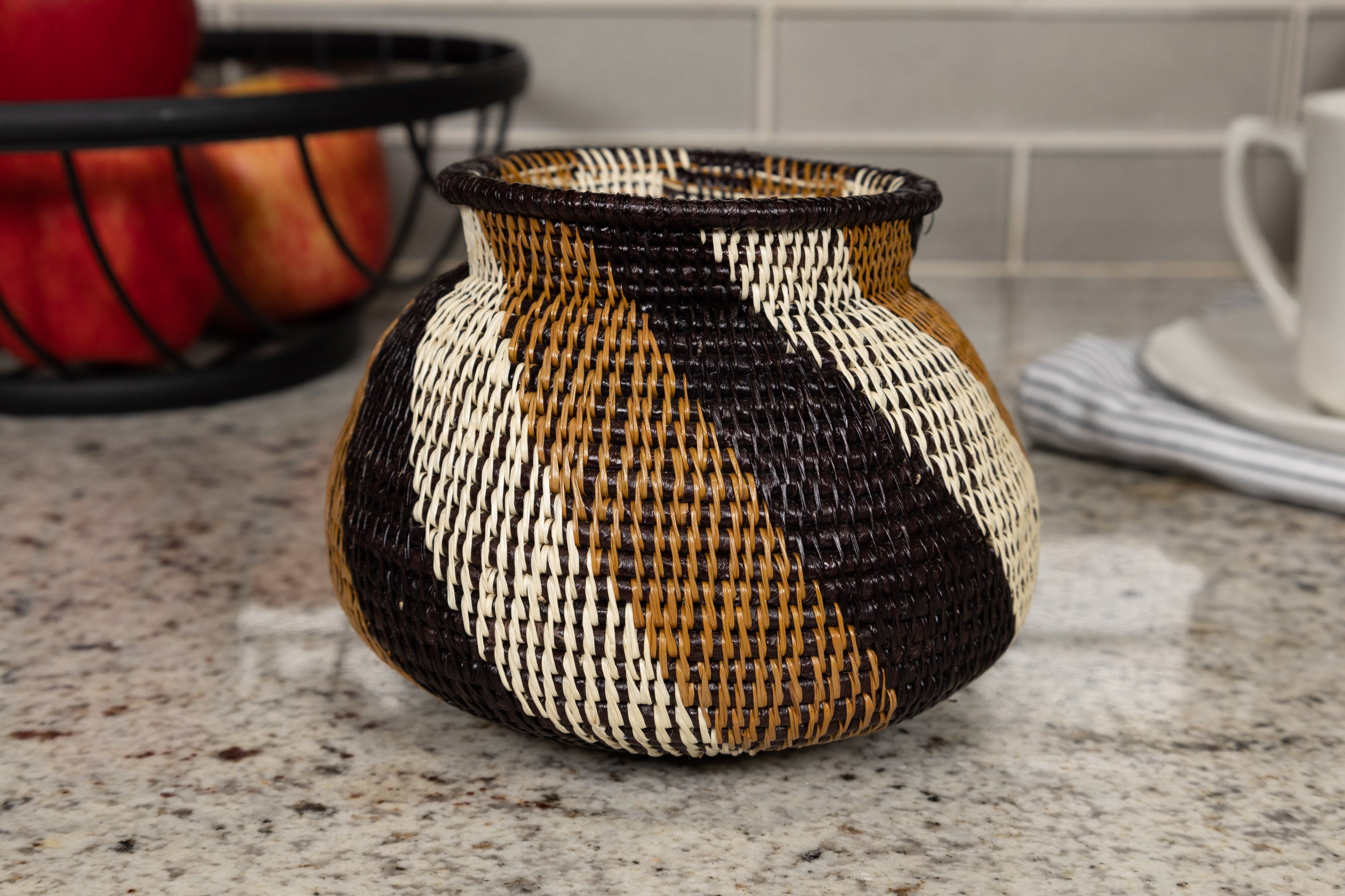Decorative woven basket with black, brown, and white pattern on a kitchen counter.