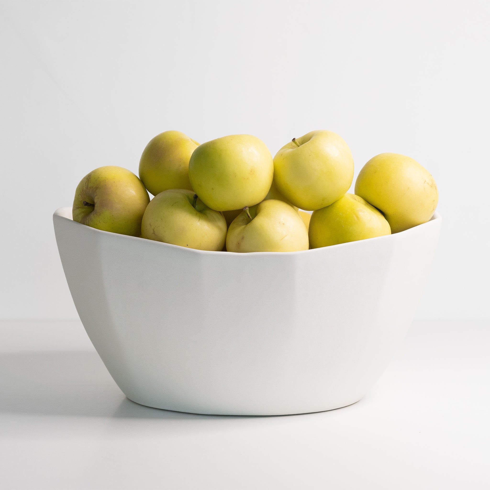 White bowl filled with green apples on a light gray background