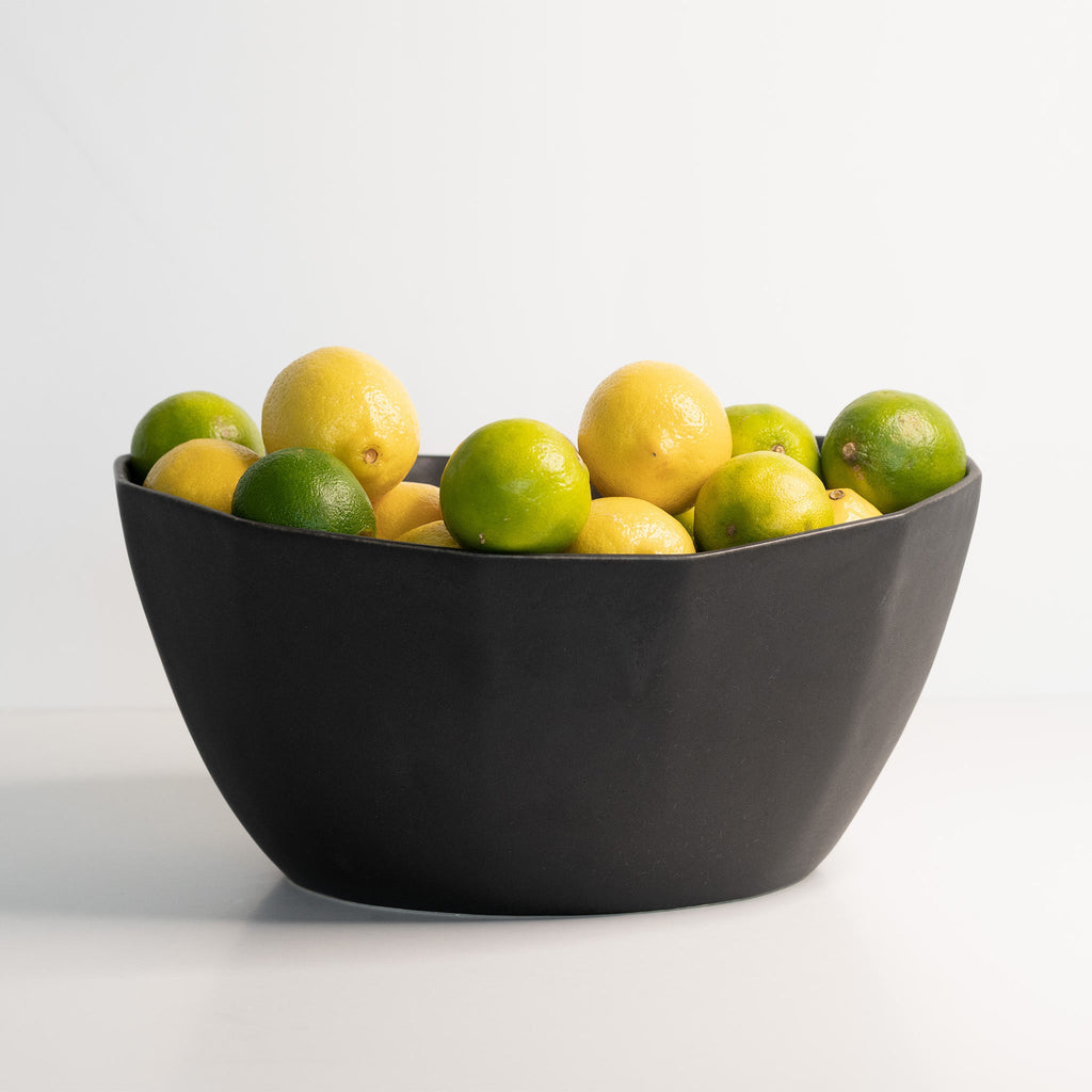 Black bowl filled with lemons and limes on a white background