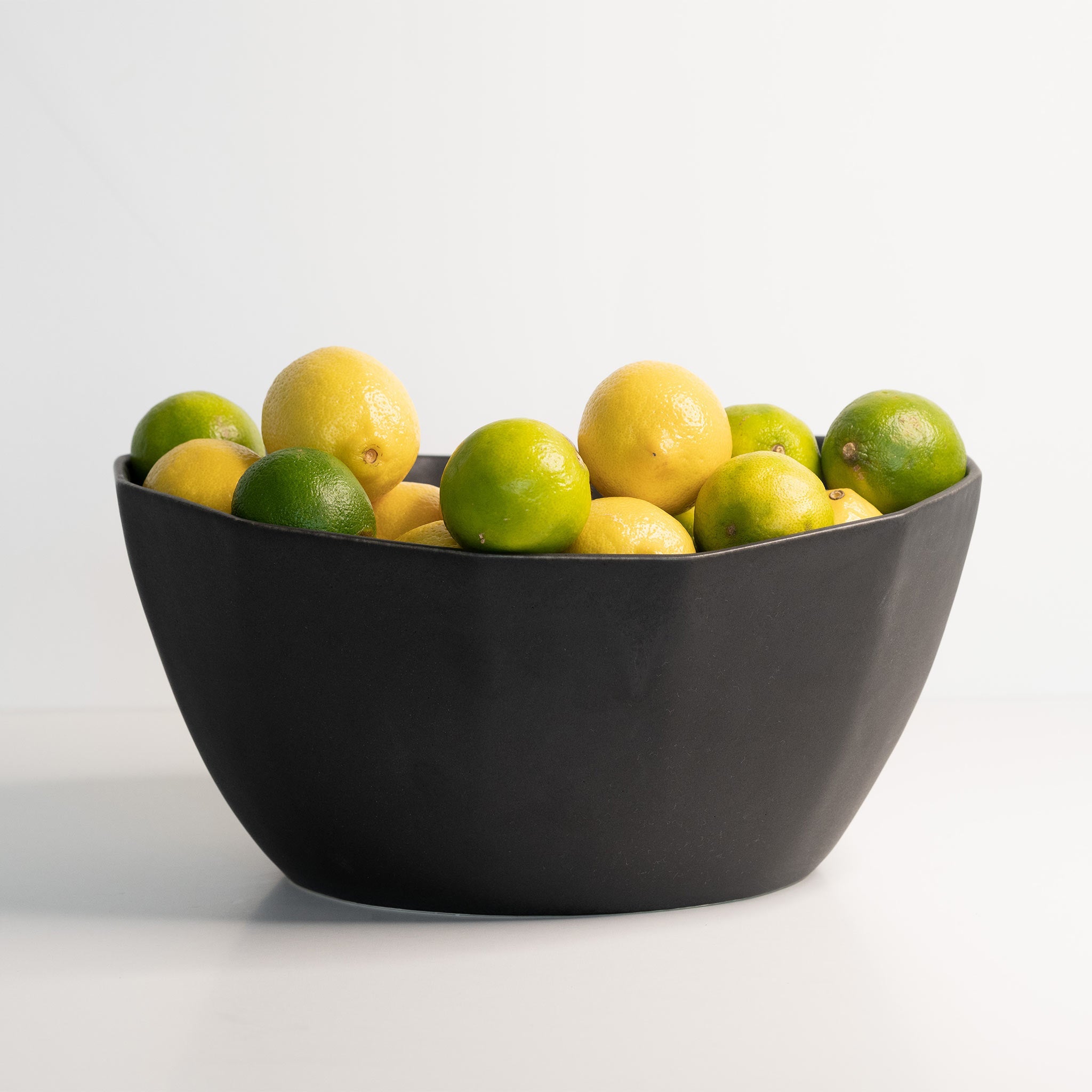 Black bowl filled with lemons and limes on a white background