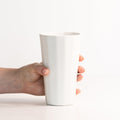 Hand holding a white ceramic cup against a white background
