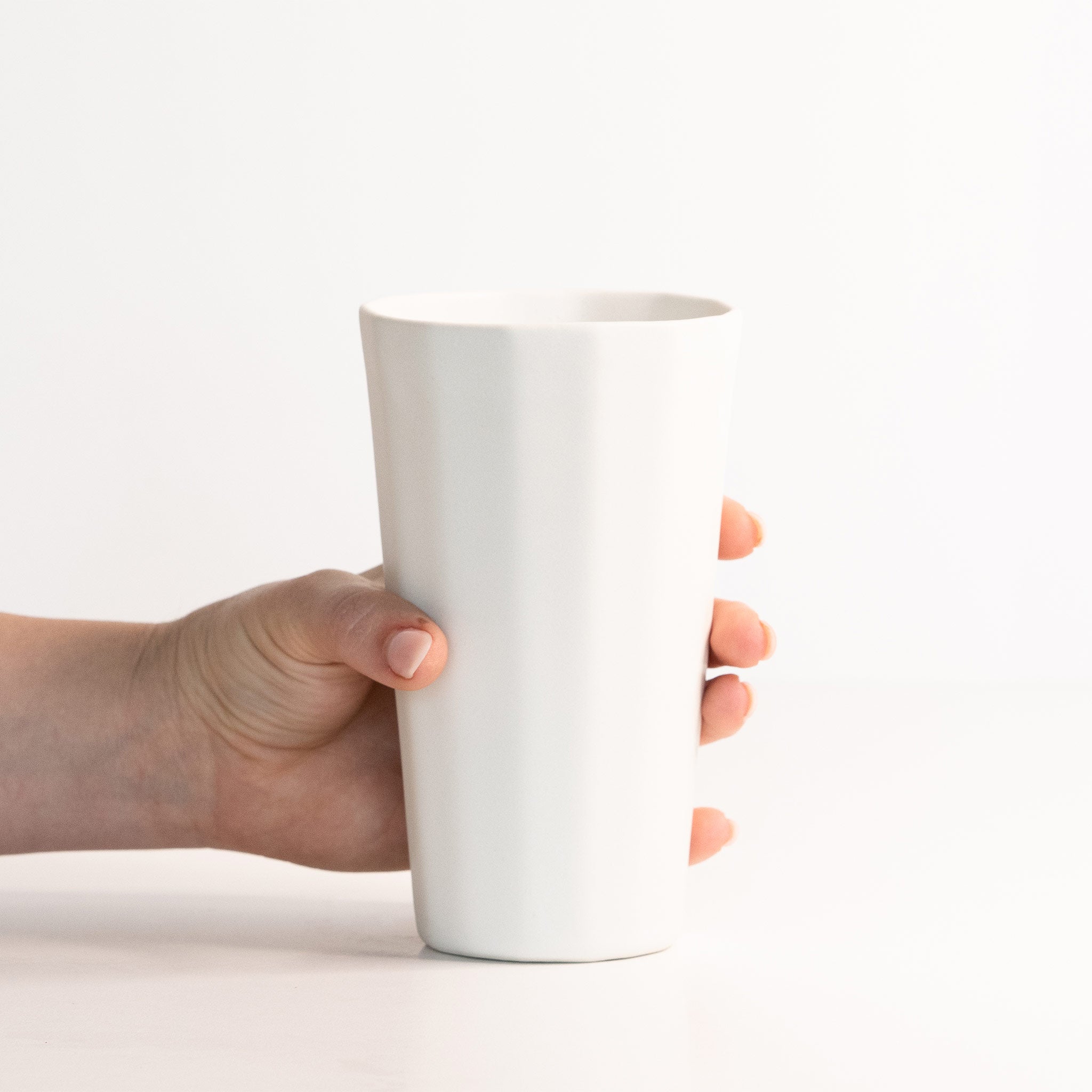 Hand holding a white ceramic cup against a white background