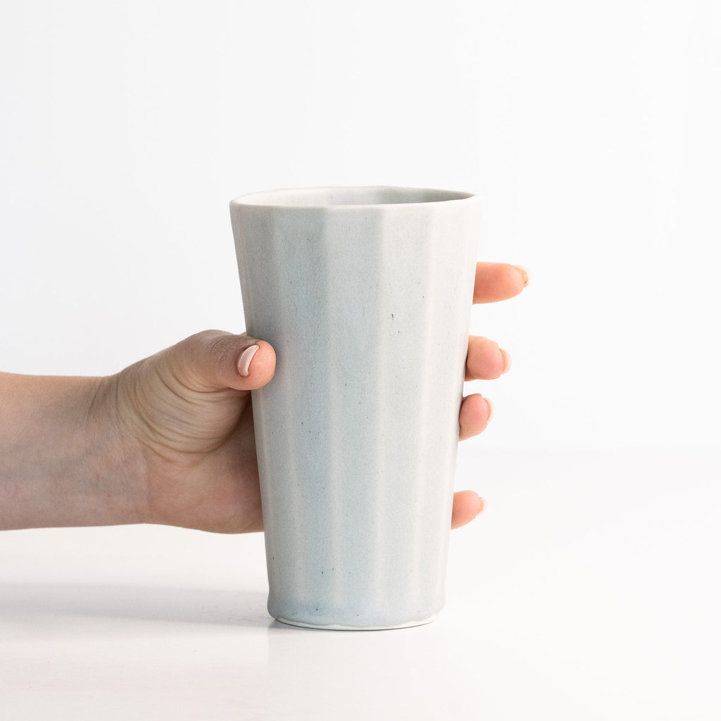 Hand holding a light gray ceramic cup on a white background