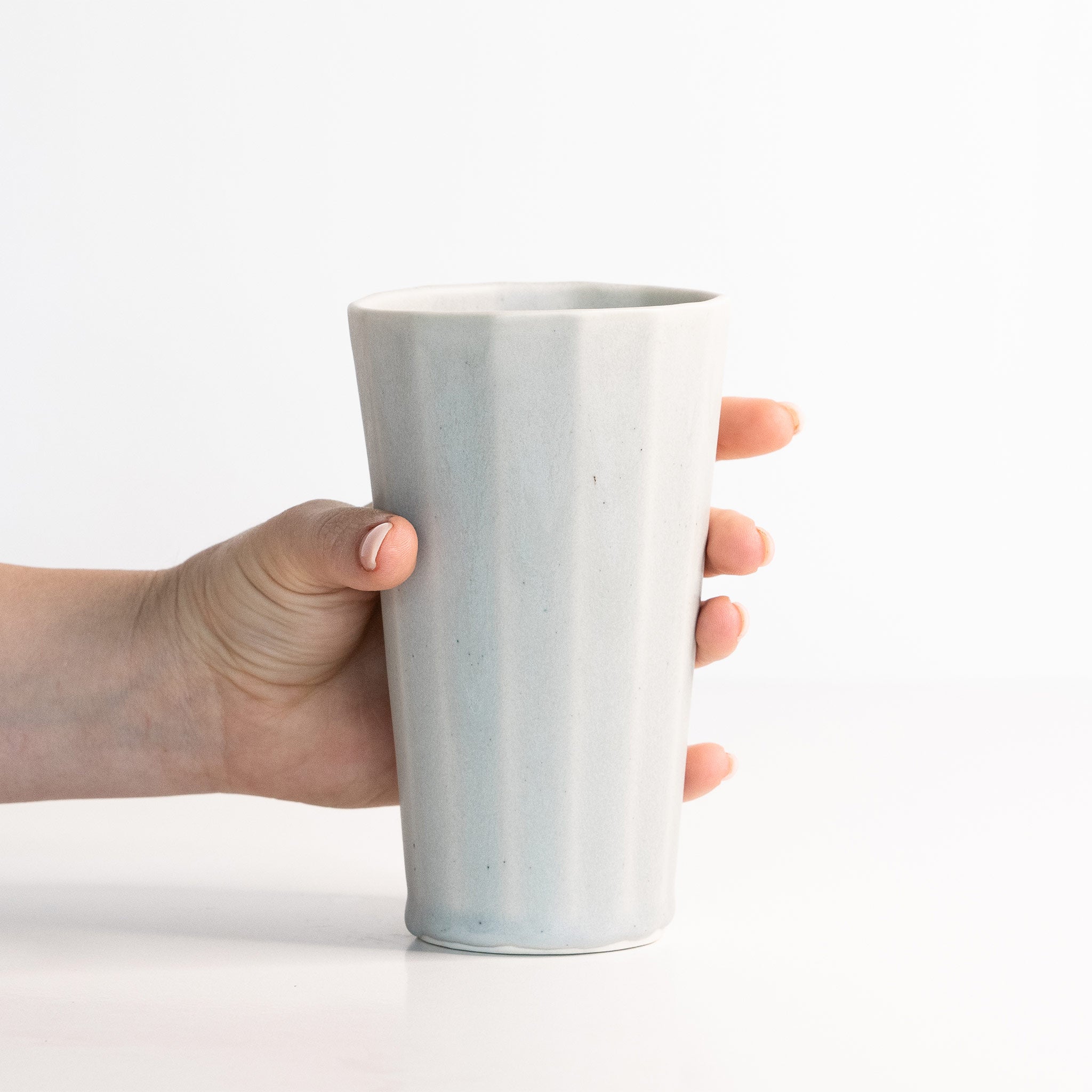 Hand holding a light gray ceramic cup on a white background