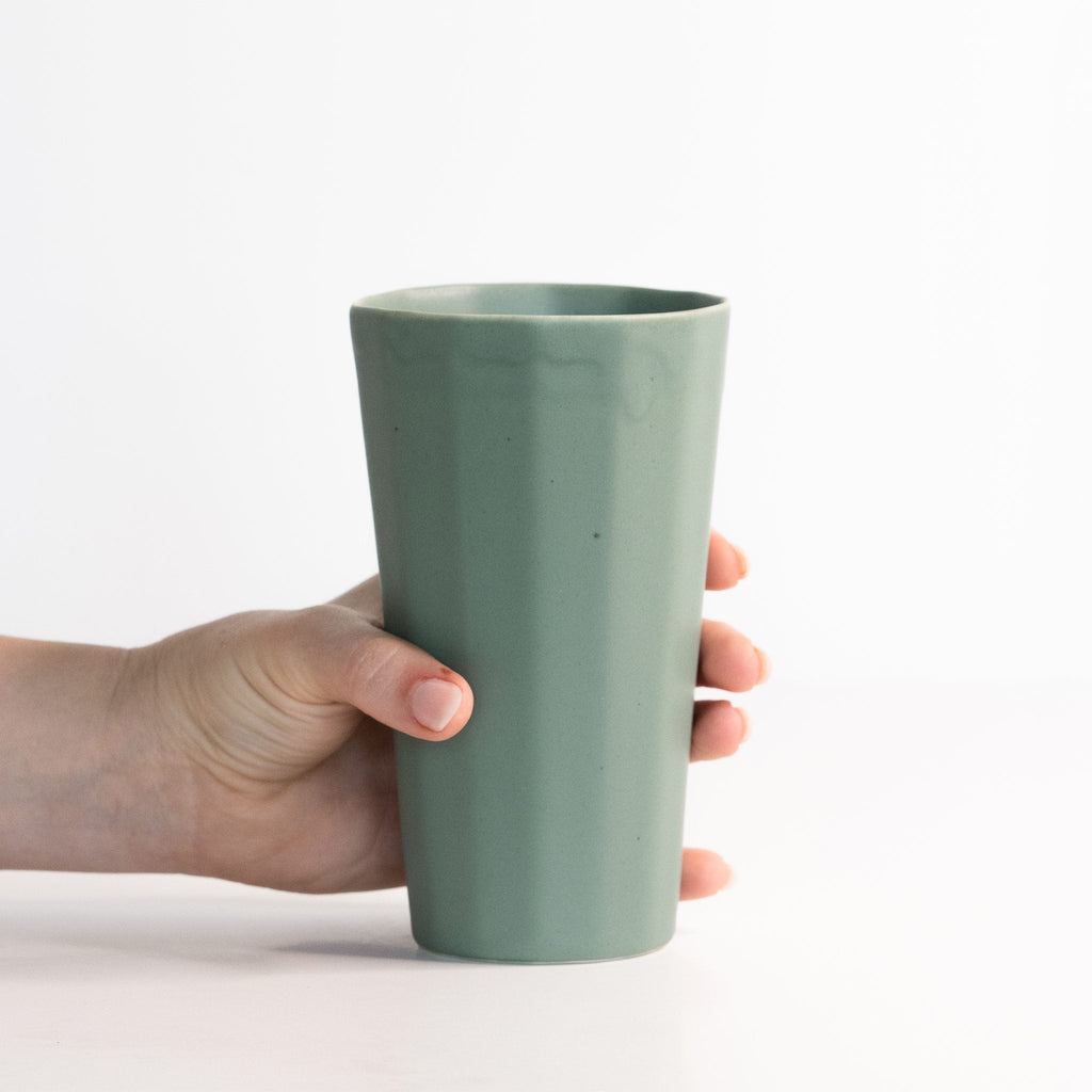 Hand holding a green ceramic cup against a white background