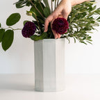 Hand arranging flowers in a white hexagonal vase on a light background