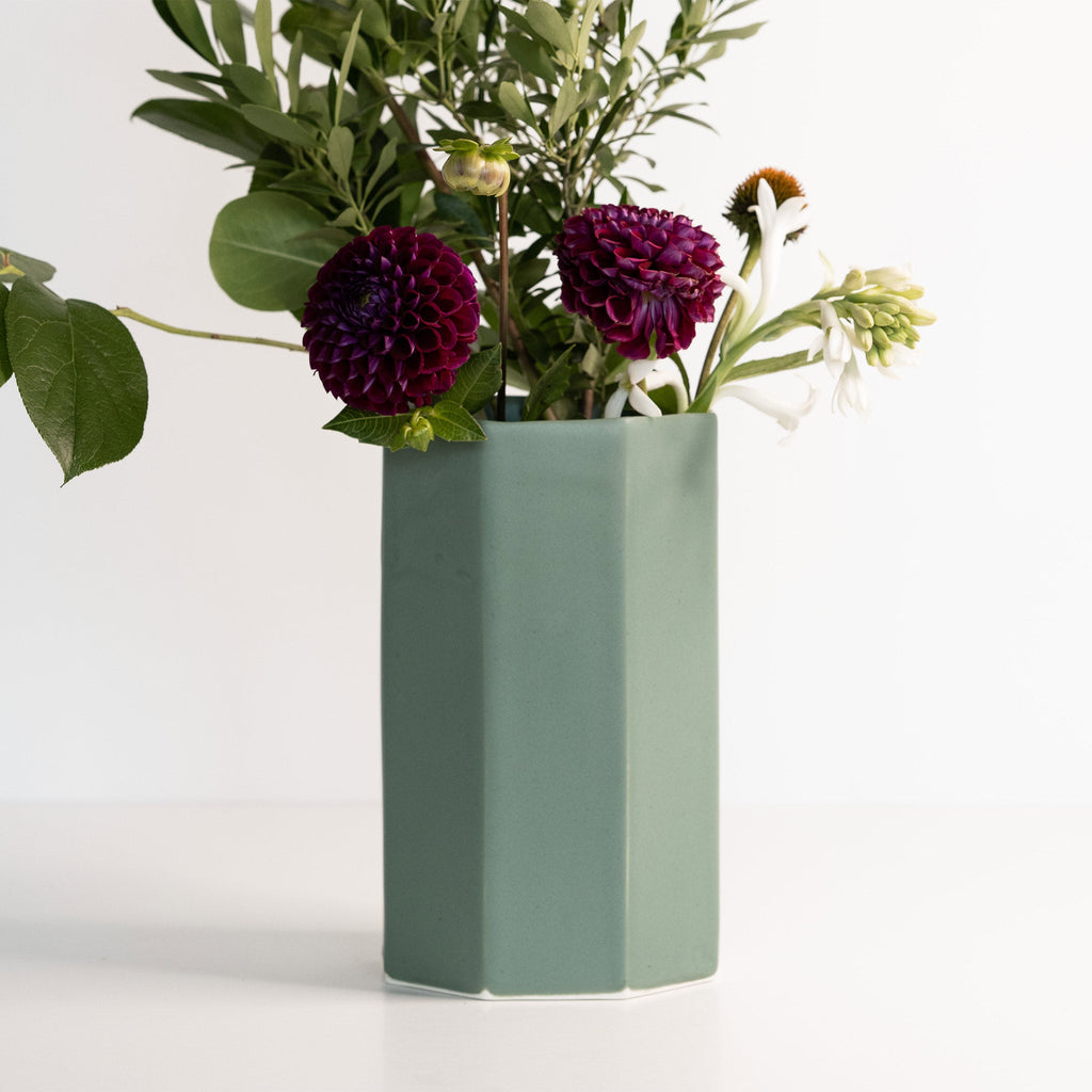 Green vase with purple flowers on a white background