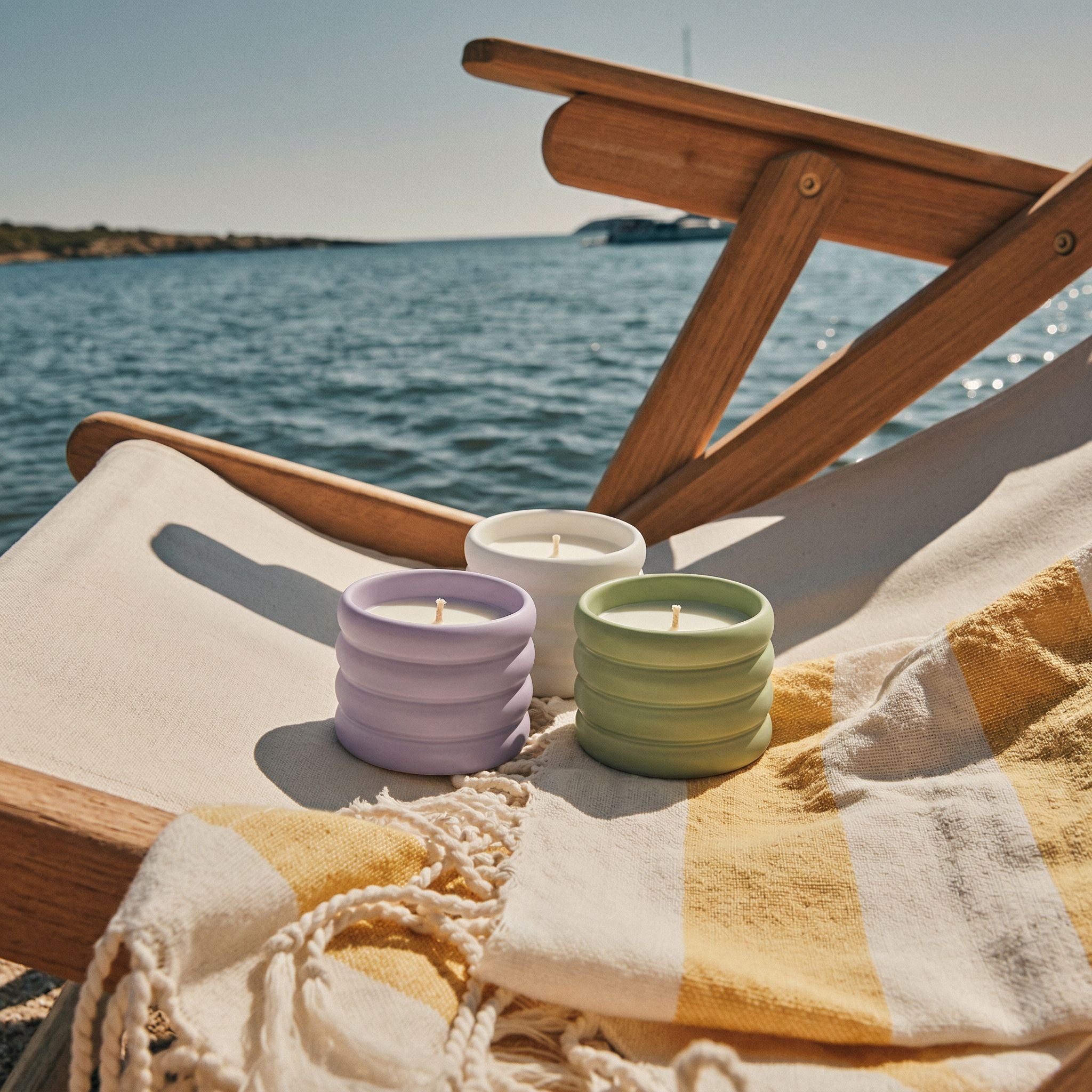 Three colorful candles on a wooden deck with a scenic ocean view.