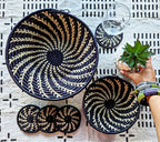 Black and gold woven baskets on a patterned tablecloth with a hand holding a plant.