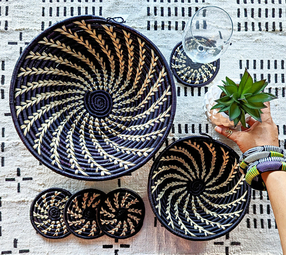 Black and gold woven baskets on a patterned tablecloth with a hand holding a plant.