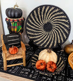 Decorative setup with pumpkins, a woven chair, and decorative plates on a black patterned surface.
