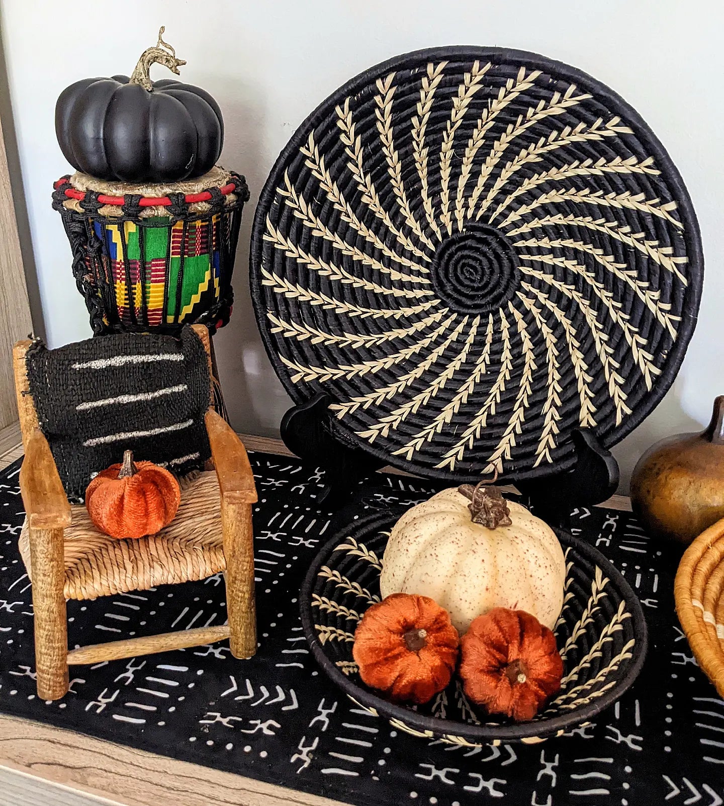 Decorative setup with pumpkins, a woven chair, and decorative plates on a black patterned surface.