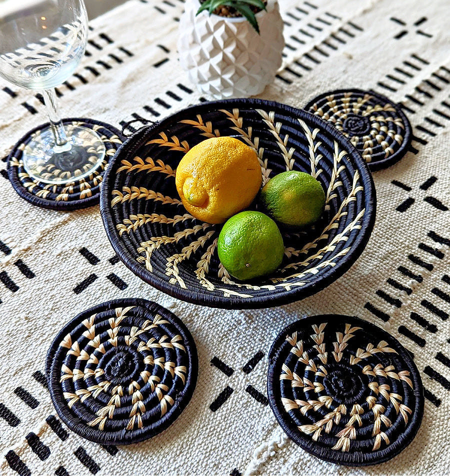 Decorative woven coasters with a bowl of lemons and limes on a patterned tablecloth.