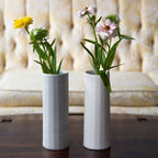 Two white vases with flowers on a wooden surface with a blurred background