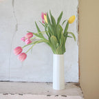 White vase with pink and yellow tulips against a textured wall.