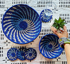 Set of blue woven coasters and bowls on a patterned surface with a hand holding a plant.