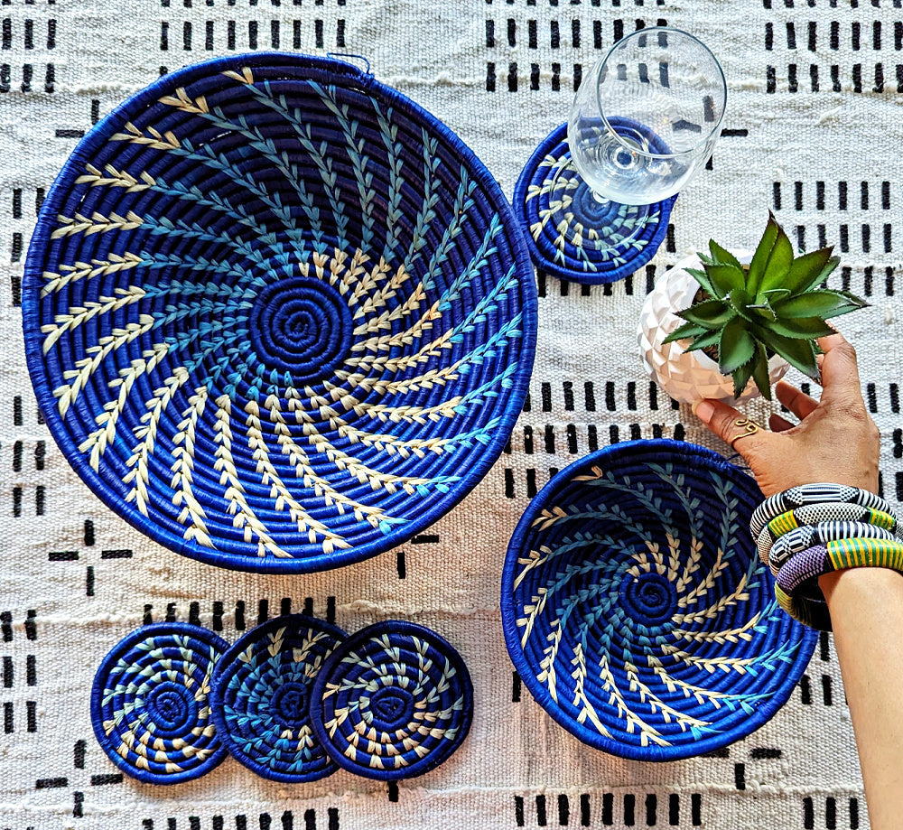 Set of blue woven coasters and bowls on a patterned surface with a hand holding a plant.