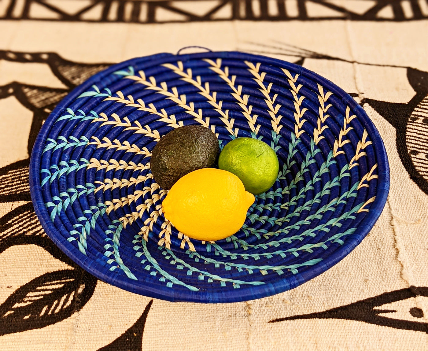 Decorative blue woven plate with a lemon, lime, and avocado on a patterned fabric background