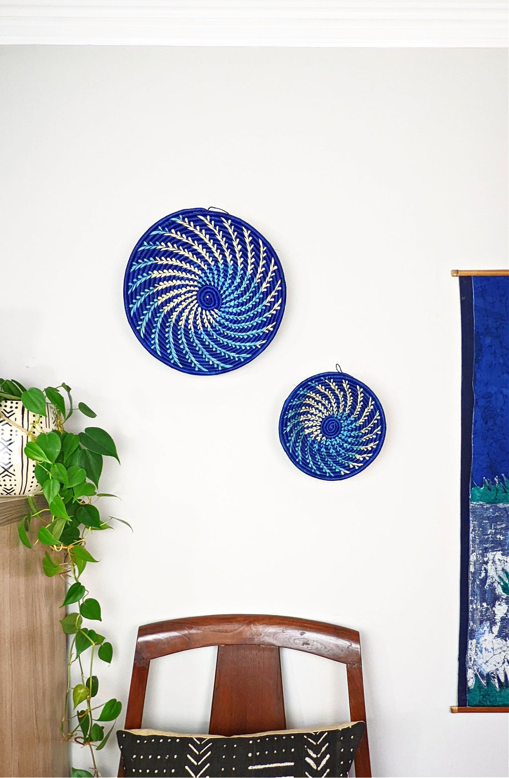 Two blue circular wall art pieces on a white wall with a chair and plant in the foreground.