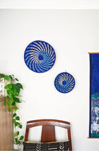 Two blue circular wall art pieces on a white wall with a chair and plant in the foreground.