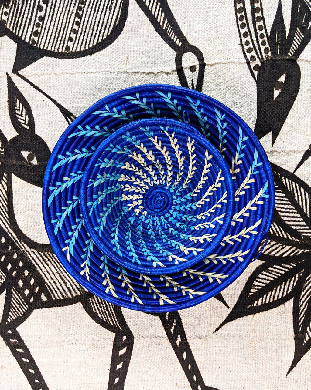 Blue woven basket with a spiral pattern on a fabric background with black and white animal illustrations.