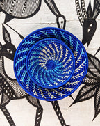 Blue woven basket with a spiral pattern on a fabric background with black and white animal illustrations.