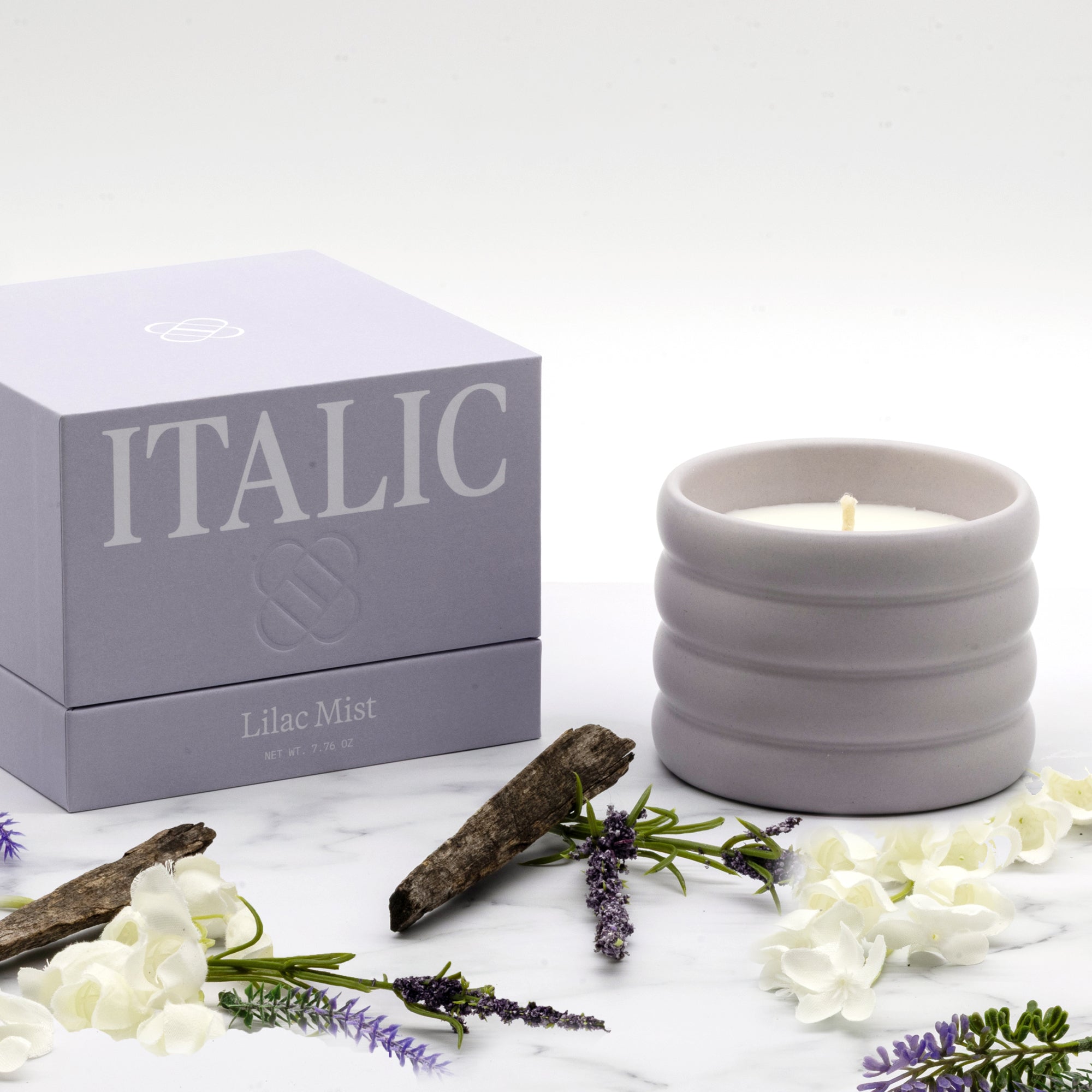 Ceramic candle with 'Italic' packaging on a white surface with flowers and branches.