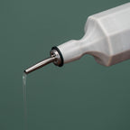 White bottle with a metal nozzle dispensing liquid on a green background