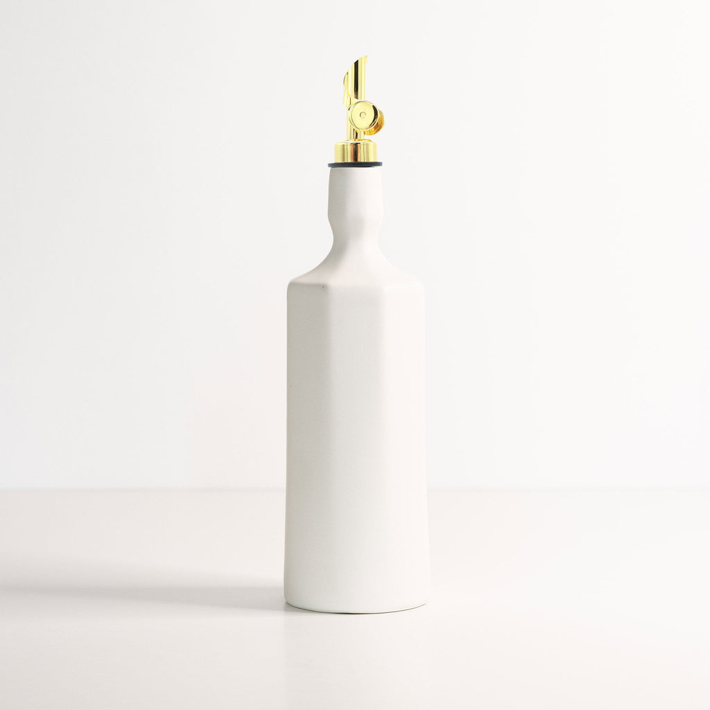 White ceramic oil dispenser with a gold nozzle on a light gray background