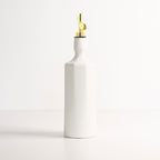 White ceramic oil dispenser with a gold nozzle on a light gray background