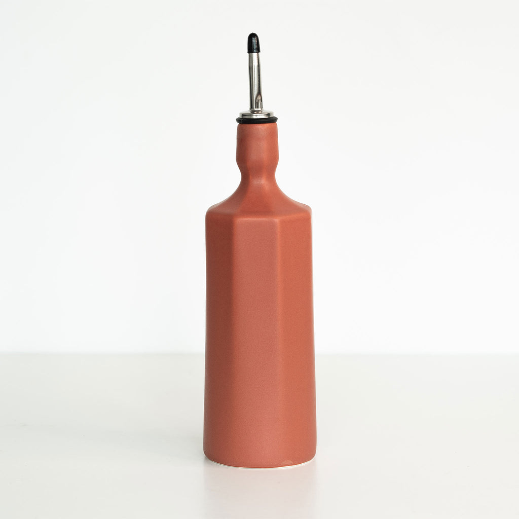 Terracotta-colored oil dispenser bottle with a black cap on a white background