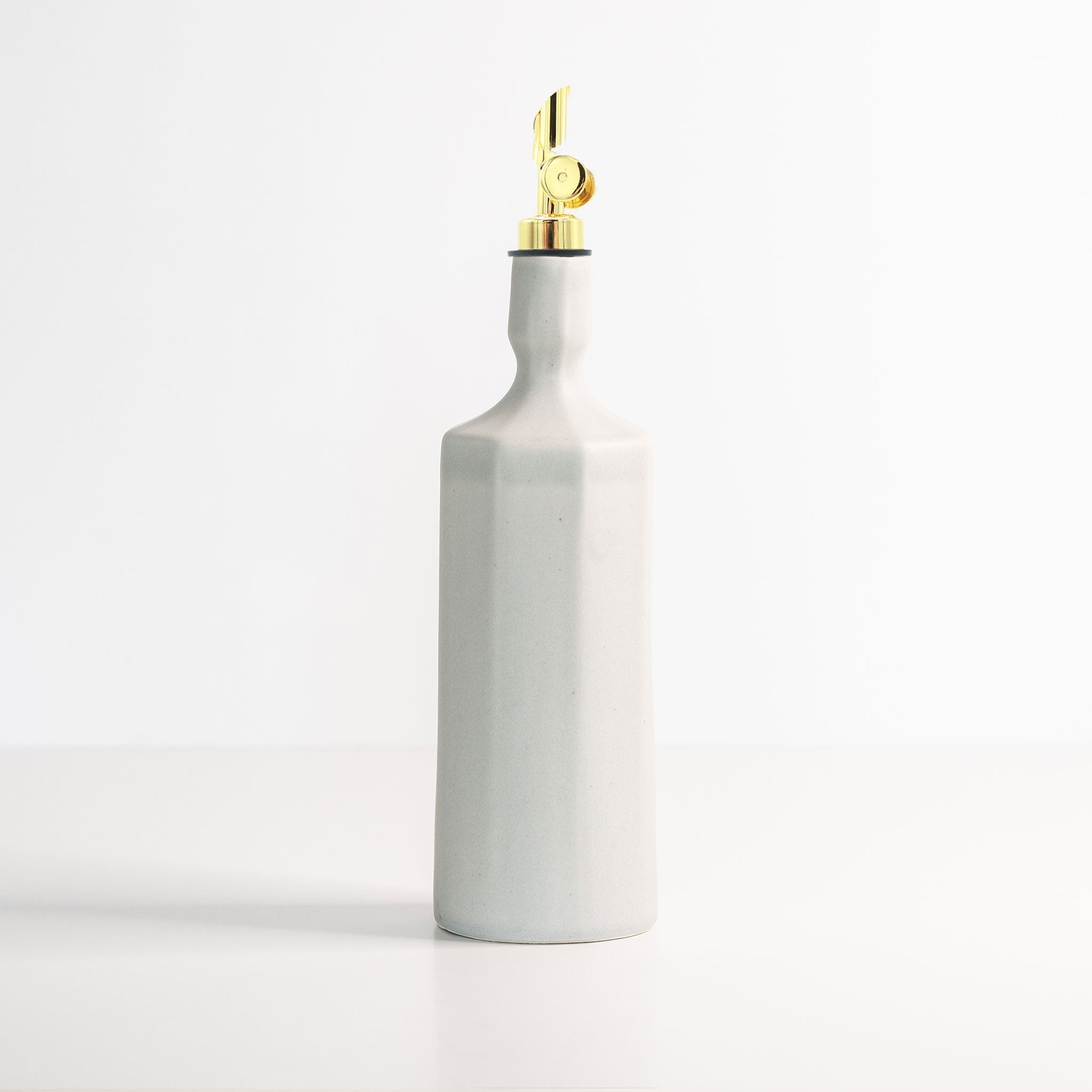 White ceramic oil dispenser bottle with gold cap on a white background
