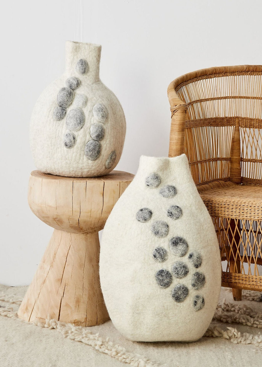 Two textured vases on a wooden stand with a wicker chair in the background.