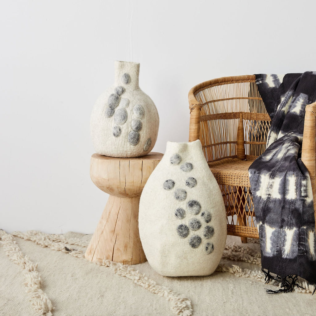 Two textured vases on a wooden stand with a wicker chair and tie-dye blanket in the background.