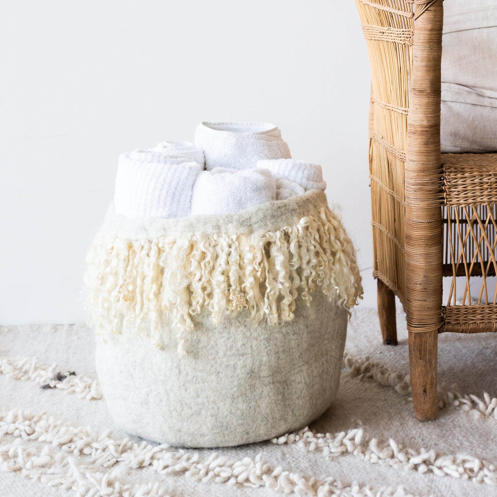 Textured vase with fringe on a rug next to a wicker chair
