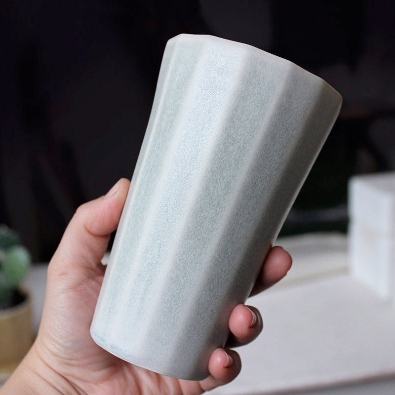 Hand holding a ceramic cup against a blurred indoor background