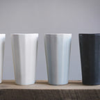 Four ceramic cups in white, gray, and black on a wooden surface with a gray background