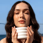 Woman's face and hands  holding a white ceramic candle against a blue sky background