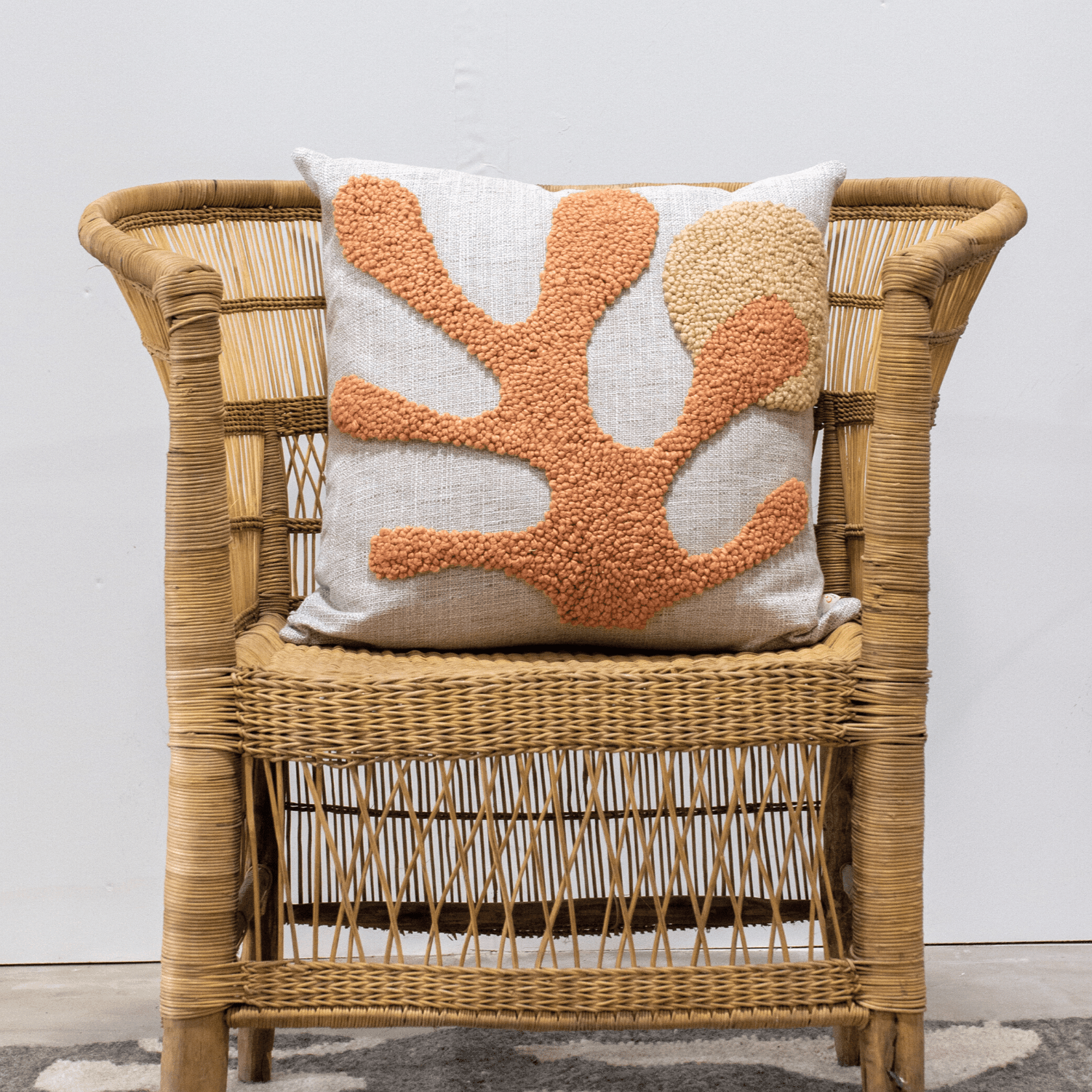 Wicker chair with a decorative pillow featuring coral design on a plain background