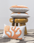 Stack of decorative pillows with coral design on a stool against a neutral background