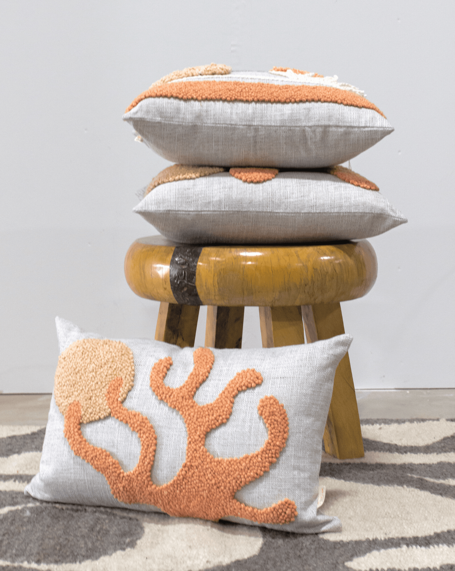 Stack of decorative pillows with coral design on a stool against a neutral background