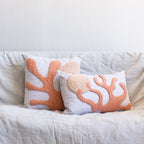 Two coral-patterned pillows on a light-colored sofa against a white wall.