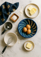 Ingredients for baking including eggs, butter, salt, and a whisk on a marble surface.