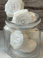 Glass jar filled with white toilet bombs labeled 'Toilet Bomb' on a wooden surface.