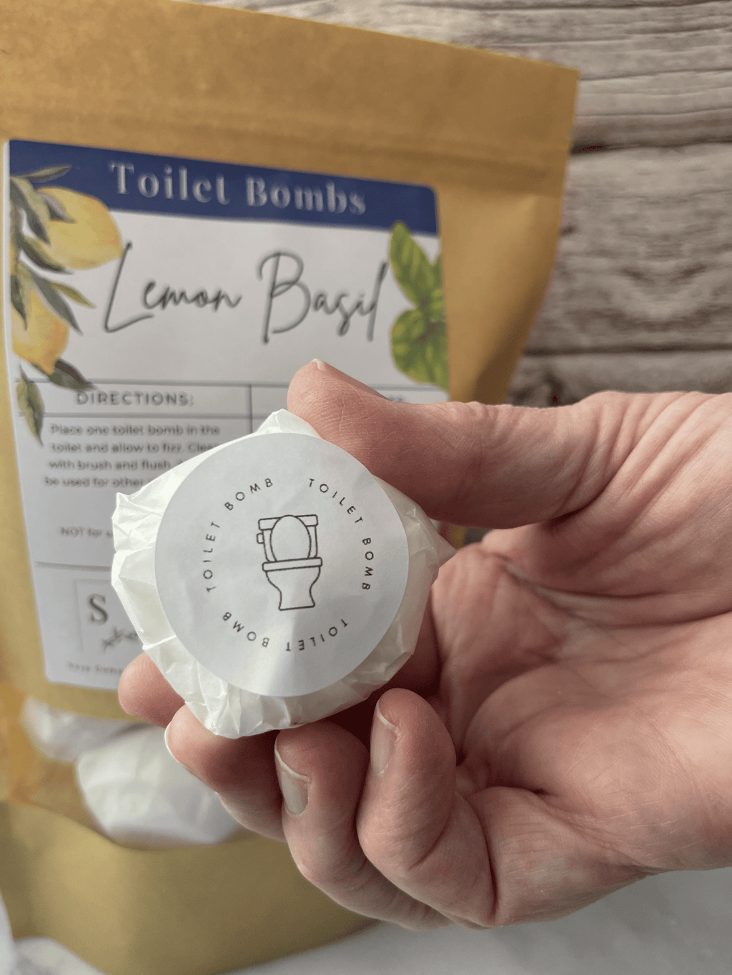 Hand holding a lemon basil toilet bomb with packaging in the background